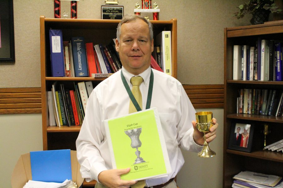Trinity teacher/counselor Mr. Mike Magre holds the Elijah Cup and information about the program.
